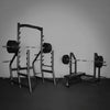 Gym equipment including a squat rack and weight bench on a dark floor with a gray wall.