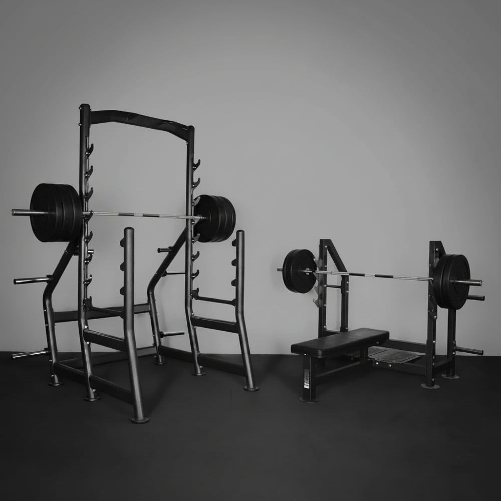 Gym equipment including a squat rack and weight bench on a dark floor with a gray wall.