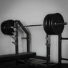 Weightlifting barbell with weights on a rack against a gray wall
