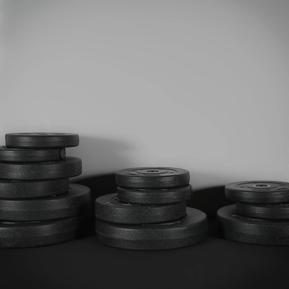 Stacks of black weight plates on a dark surface with a neutral background