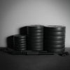 Stacks of weight plates and a barbell on a dark surface with a neutral background