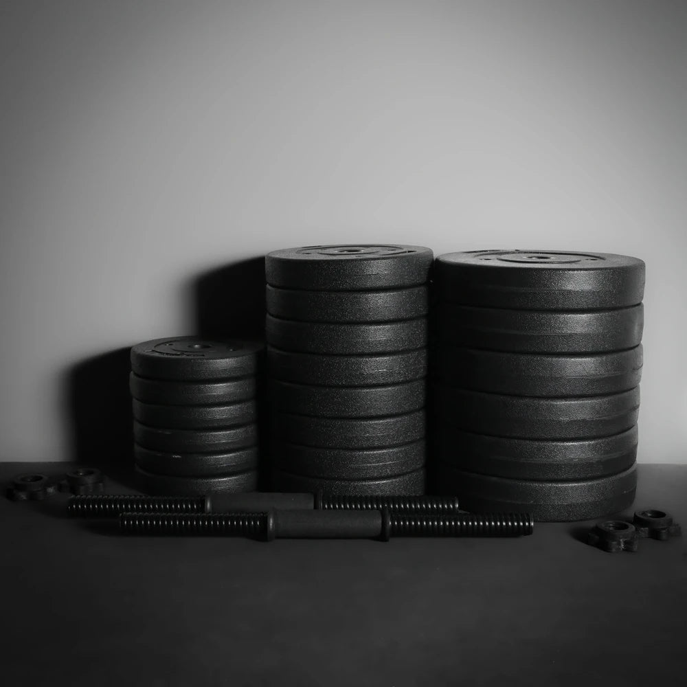 Stacks of weight plates and a barbell on a dark surface with a neutral background
