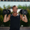 Man lifting dumbbells outdoors with a blurred natural background