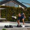 Man exercising with dumbbells outdoors on a wooden deck.