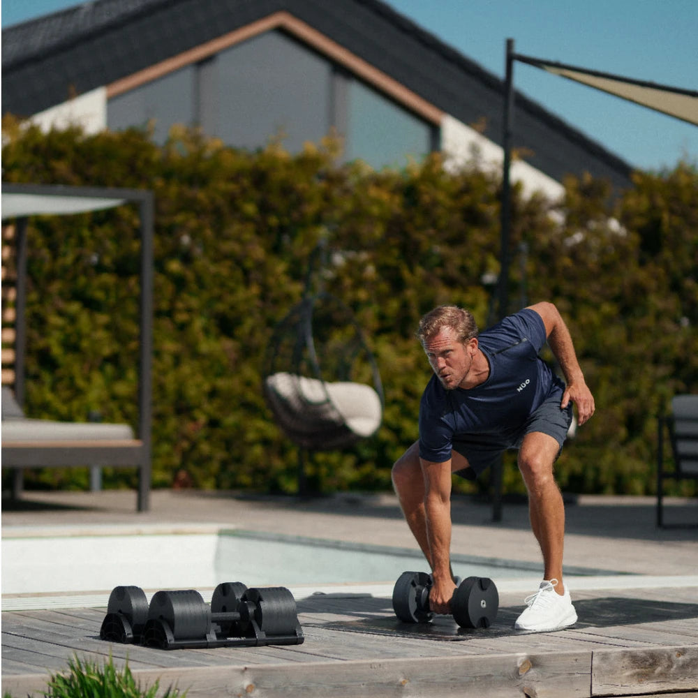 Man exercising with dumbbells outdoors on a wooden deck.