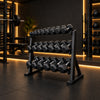 A black three-tier dumbbell rack holding multiple hex dumbbells, positioned in a gym setting with a black floor.