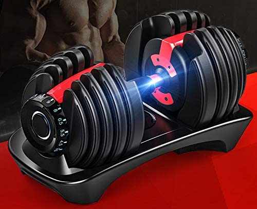 Adjustable dumbbells in a black and red color scheme, resting on a matching black stand. The background is dark with a blurred muscular torso, and the stand sits on a bright red surface.