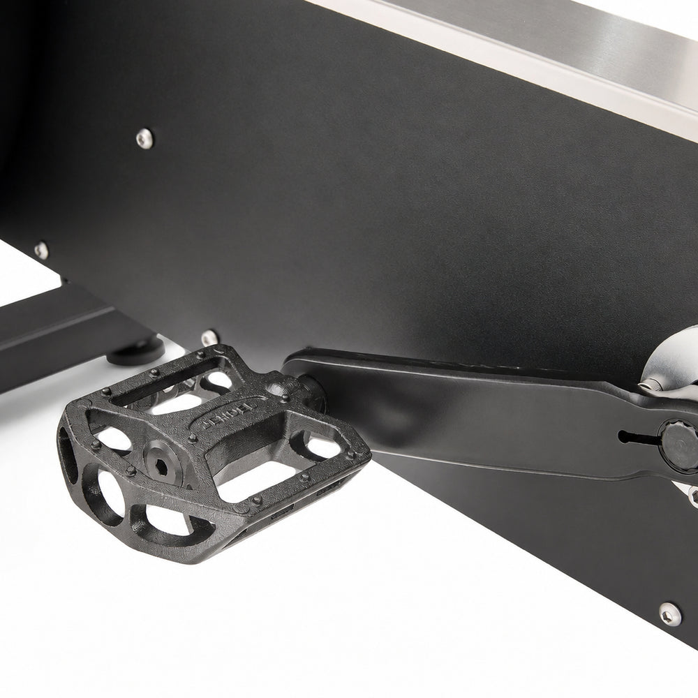Close-up of exercise bike showing a black metal pedal and part of the silver flywheel against a white background.