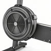 Close-up of a half-integer rowing machine with a matte black flywheel, fan grille, and part of the black frame on a white background.
