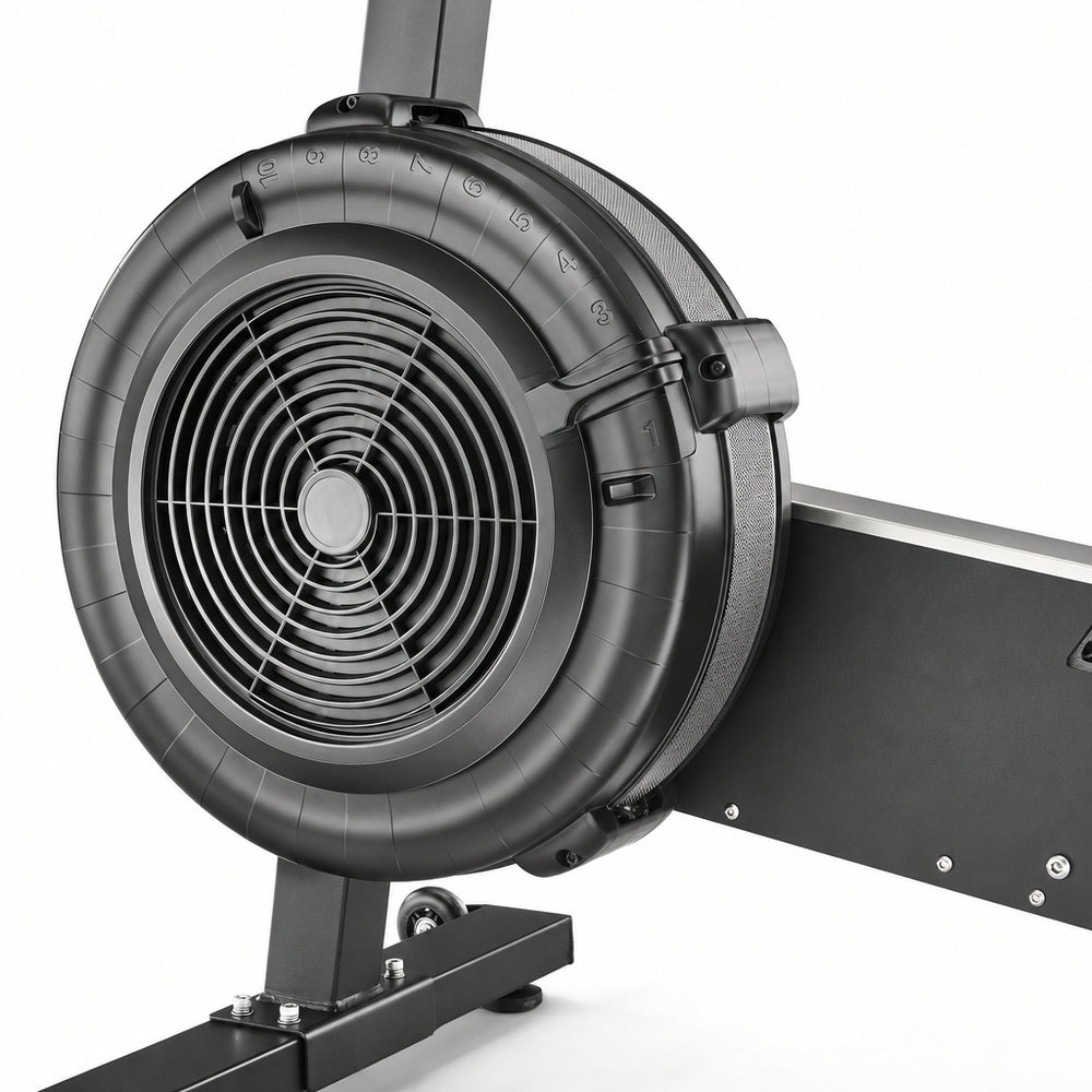 Close-up of a half-integer rowing machine with a matte black flywheel, fan grille, and part of the black frame on a white background.