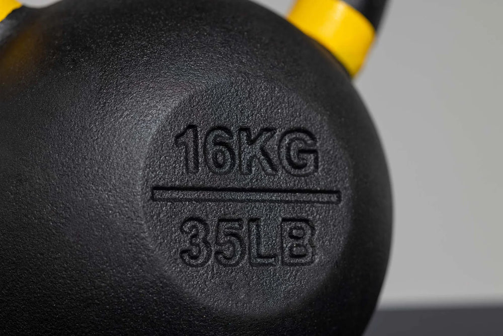 Close-up of a black cast iron kettlebell with '16KG 35LB' embossed on the side, showing a yellow and black handle against a neutral gray background.