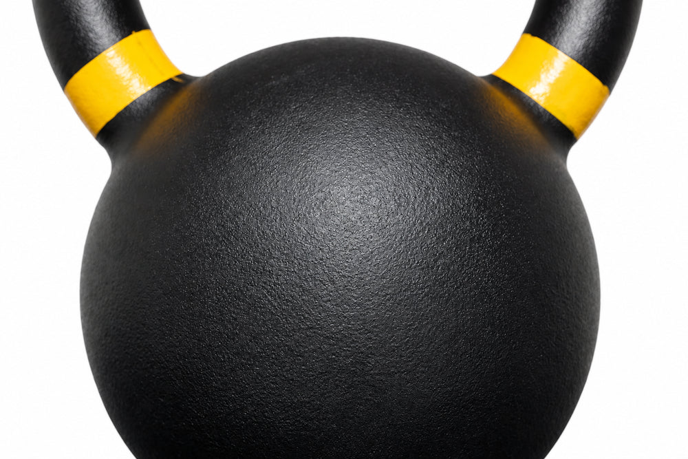 Close-up of a black kettlebell with yellow bands on the handles against a white background.