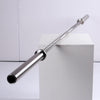 A silver metal barbell resting diagonally across a white display block against a light gray studio background.