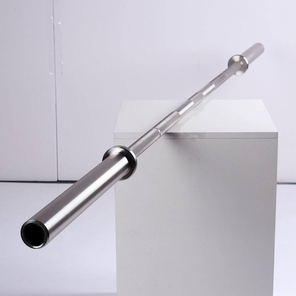 A silver metal barbell resting diagonally across a white display block against a light gray studio background.