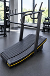 A black curved treadmill with yellow trim and dual handlebar cradles.