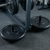 Close-up of a black metal weight bench frame with weight plates on the floor in a gym setting.