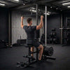 A black multi-functional home gym cable machine with a backrest, seat, pulldown handles, and a high pull-up bar, shown on a solid white background.