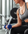 A woman in a gray sports bra and black leggings holds a blue hex dumbbell 