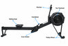 An air rower exercise machine shown on a white background with labeled callouts pointing to the monitor, fan flywheel, sliding seat, handlebar, foot holder, and pulley wheel.