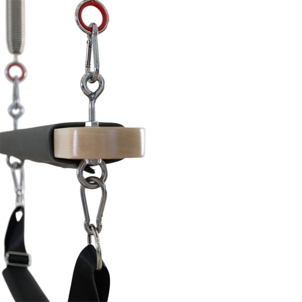 Close-up of the wooden bar end cap and carabiner clips on the Cadillac reformer trapeze
